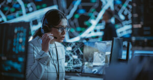 A woman sits in front of a computer screen monitoring threats in a security operations center